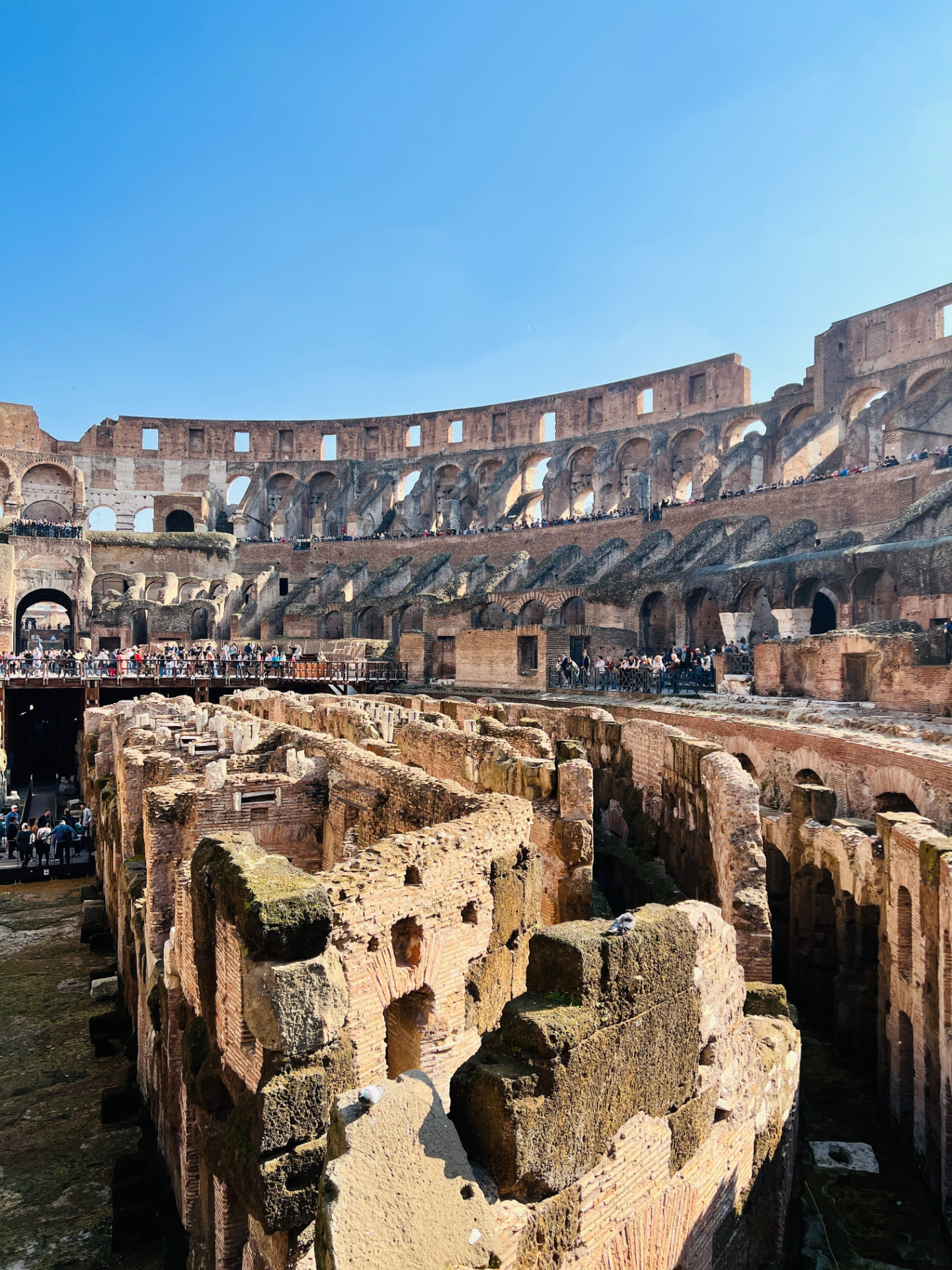 Interior of the Colosseum in Rome showing the exposed arena substructures and tiered arcades under a blue sky